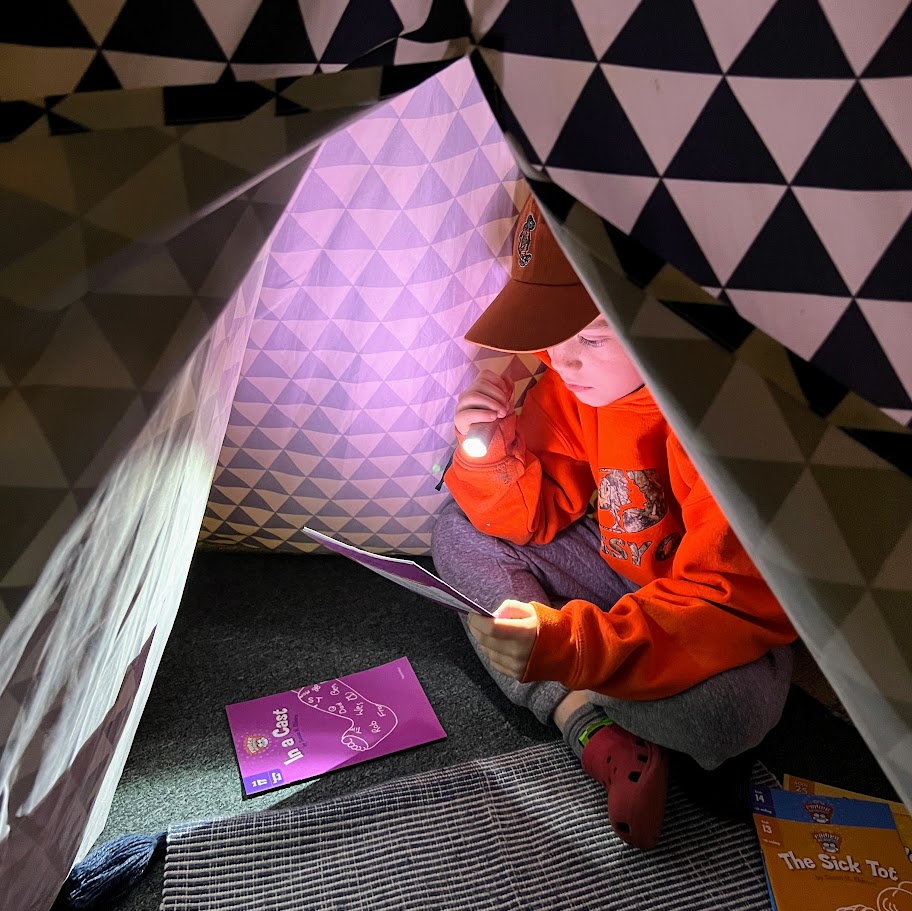 A student reads in a tent with a flashlight.